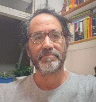 Homem branco de óculos e barba, vestindo uma camisa cinza