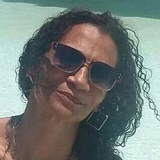 Mulher parda, de cabelos cacheados longos e óculos escuro