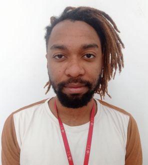 Homem negro de barba e cabelos de trança, vestindo camisa branca com marrom