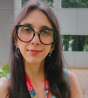 Mulher branca de cabelos negros longos, portanto óculos, vestindo uma camiseta azul.