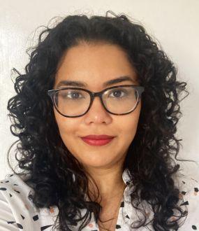 Mulher branca de cabelos cacheados escuro, usando óculos e vestindo uma blusa branca
